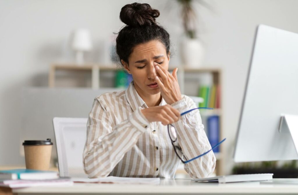 An office worker rubbing their dry irritated eyes after working long hours in front of their computer.