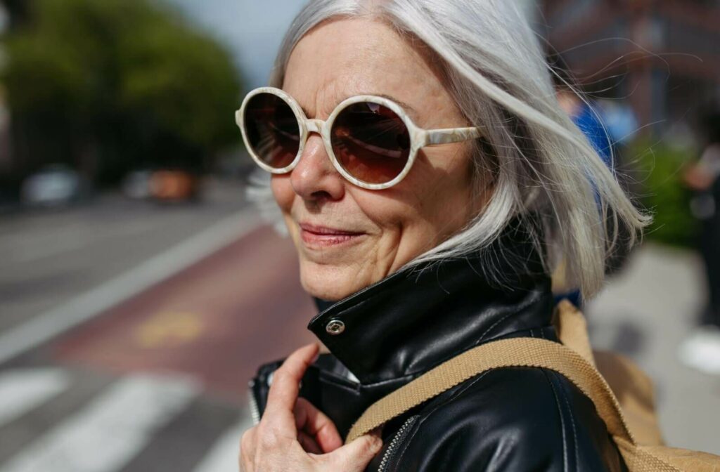 A stylish older person wearing round white sunglasses on a city street.